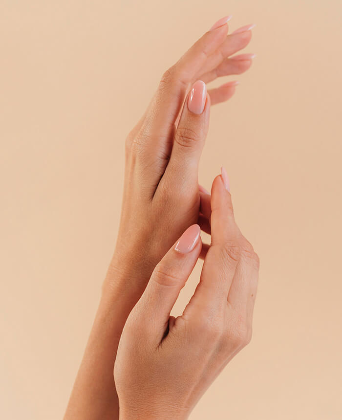 Mão de uma cliente com unhas de acrílico rosa e decoração floral.